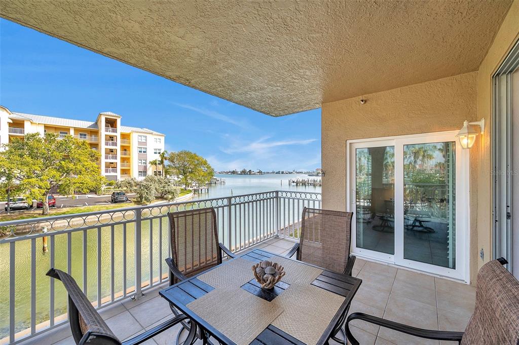 A balcony with a dining set overlooks a canal and a multi-story apartment building — 399 150TH AVENUE UNIT 101, MADEIRA BEACH, FL
