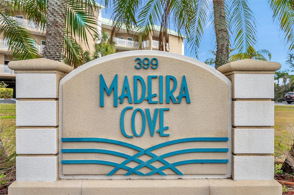 A beige monument sign with blue lettering reads Madeira Cove 399 in front of buildings — 399 150TH AVENUE UNIT 101, MADEIRA BEACH, FL