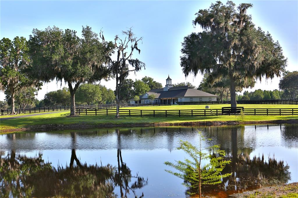 A large barn with a cupola sits behind a fenced pasture and a reflective pond — 13375 W HIGHWAY 318, WILLISTON, FL