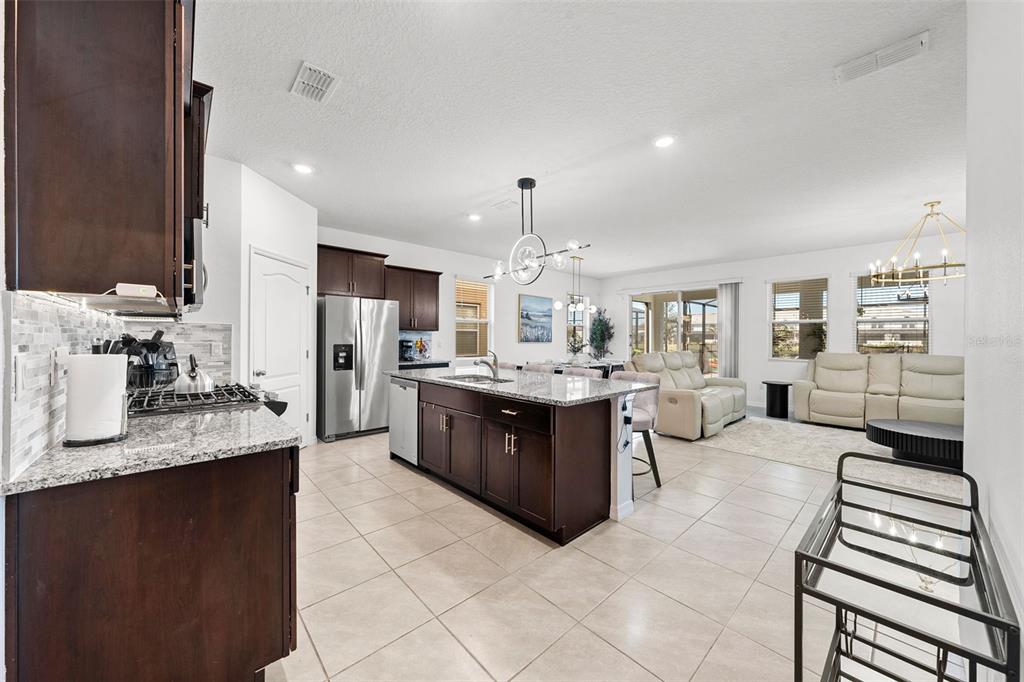 An open-concept kitchen with dark cabinets and a granite island overlooks a living area — 7552 OAKMOSS LOOP, DAVENPORT, FL