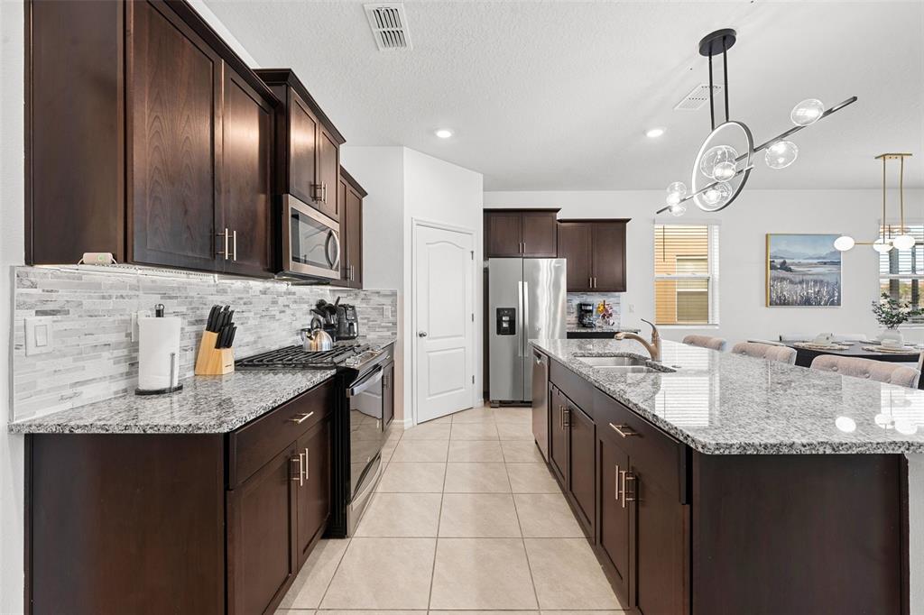 A kitchen features dark wood cabinets, granite countertops, stainless steel appliances, and a central island — 7552 OAKMOSS LOOP, DAVENPORT, FL