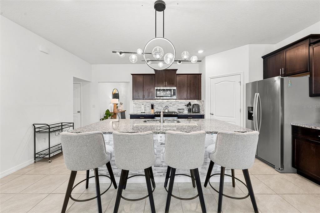 A kitchen features a large granite-topped island with four gray stools and dark cabinetry — 7552 OAKMOSS LOOP, DAVENPORT, FL