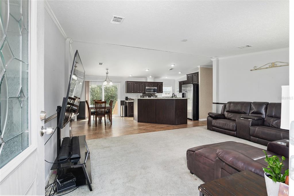 An open-concept living room with carpeted floors flows into a kitchen with dark wood cabinets — 14785 SW 71ST AVENUE ROAD, OCALA, FL