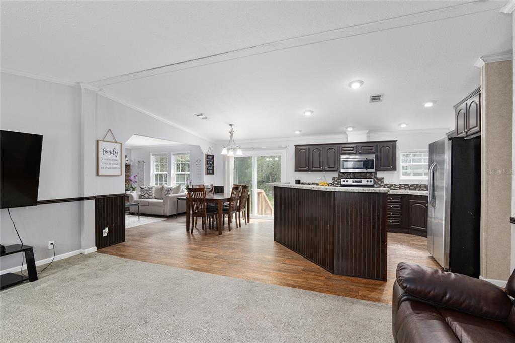 An open-concept living area features a carpeted living room, dining space, and kitchen with dark cabinetry — 14785 SW 71ST AVENUE ROAD, OCALA, FL