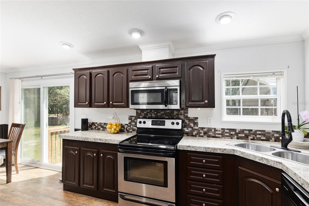 A kitchen features dark wood cabinets, stainless steel appliances, a mosaic backsplash, and granite countertops — 14785 SW 71ST AVENUE ROAD, OCALA, FL
