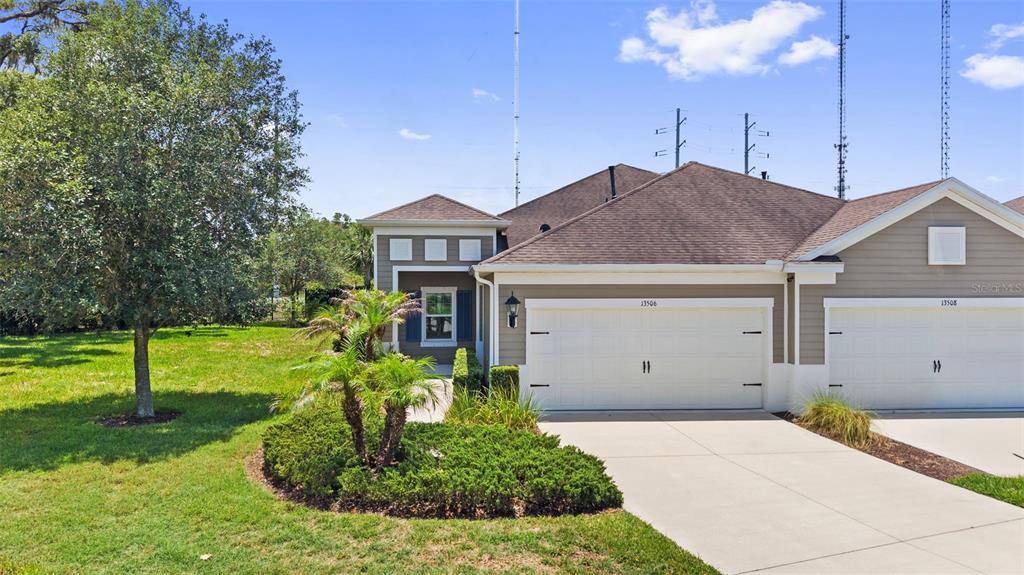 A view of the exterior of a tan duplex with white garage doors and landscaping — 13506 CIRCA CROSSING DRIVE, LITHIA, FL