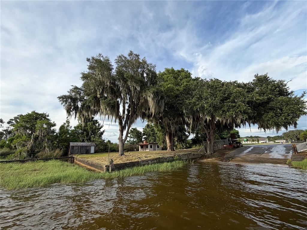 A small house sits on a waterfront lot with large trees and a boat ramp — 12703 CR-48, ASTATULA, FL
