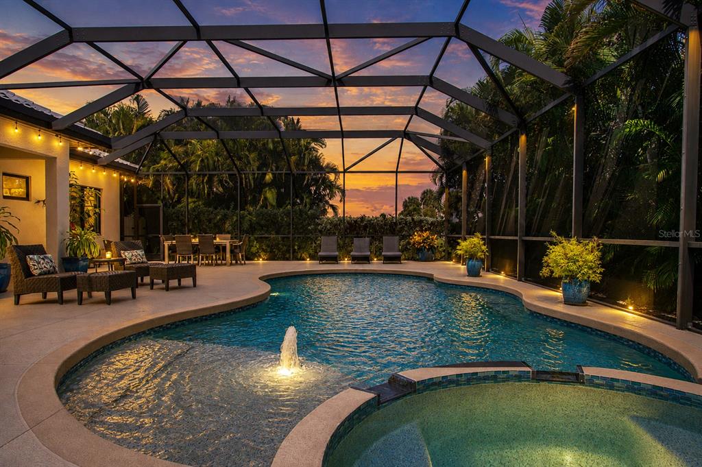A screened-in pool area with a hot tub, fountain, and patio furniture at sunset — 1929 24TH STREET CIRCLE W, PALMETTO, FL