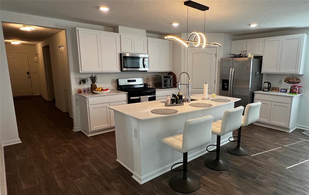 A kitchen features white cabinetry, a central island with bar stools, and dark wood flooring — 319 ARDILA CIRCLE, ST AUGUSTINE, FL