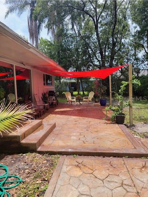 A stamped concrete patio features a red shade sail and outdoor seating next to a house — 9434 BEAR LAKE ROAD, APOPKA, FL