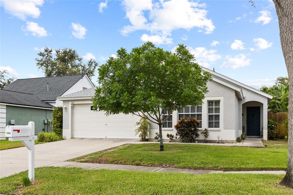 A single-story house with a white garage, gray exterior, and a front yard with trees — 1702 MEADOW OAK LANE, TARPON SPRINGS, FL