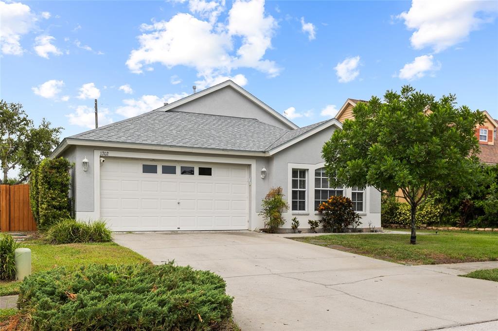 A single-story house with a white garage door, gray siding, and a concrete driveway — 1702 MEADOW OAK LANE, TARPON SPRINGS, FL