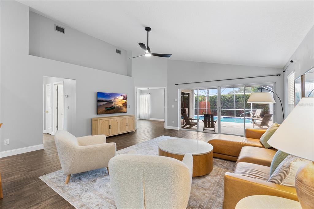 A living room with light gray walls, wood-look flooring, a vaulted ceiling, and sliding glass doors — 1702 MEADOW OAK LANE, TARPON SPRINGS, FL