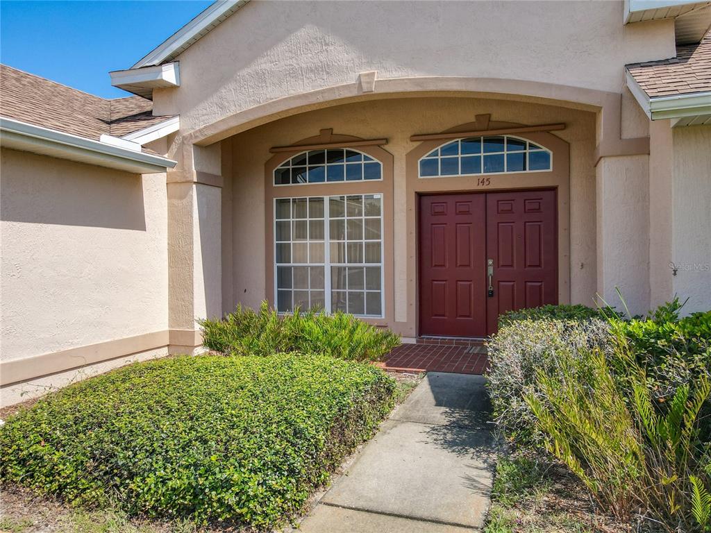 The exterior of a house features a red double front door and a large arched window — 145 NEEDLEWOOD LOOP, DEBARY, FL