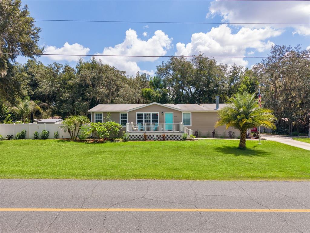 A single-story house with tan siding, a front deck, and a palm tree on the lawn — 40316 GRAYS AIRPORT ROAD, LADY LAKE, FL