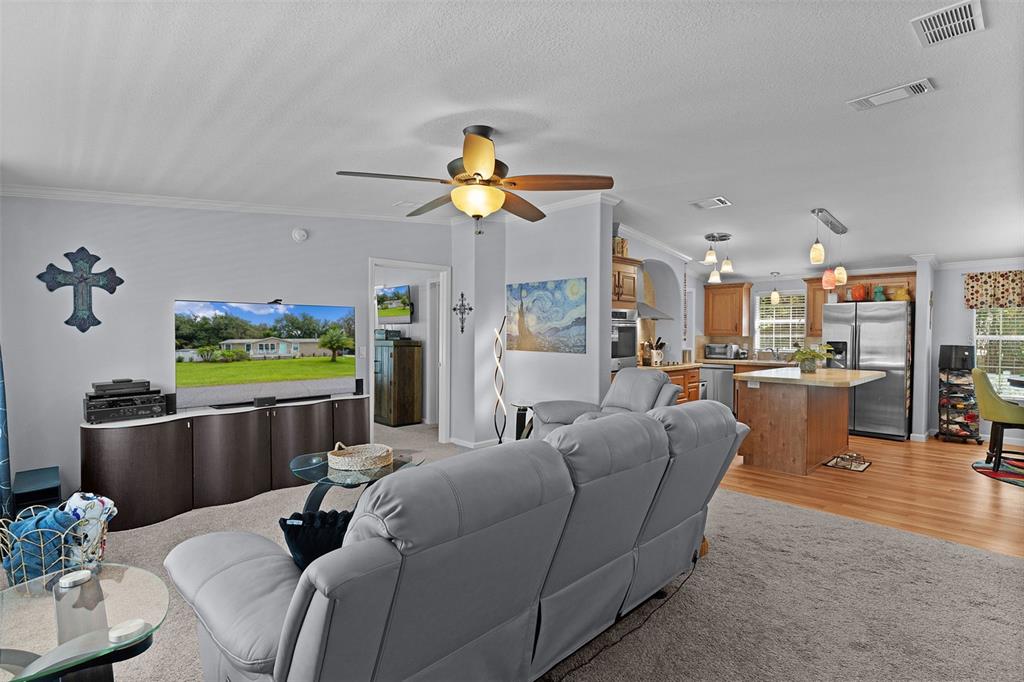 A living room with gray carpet and furniture flows into an open kitchen with wood cabinets — 40316 GRAYS AIRPORT ROAD, LADY LAKE, FL