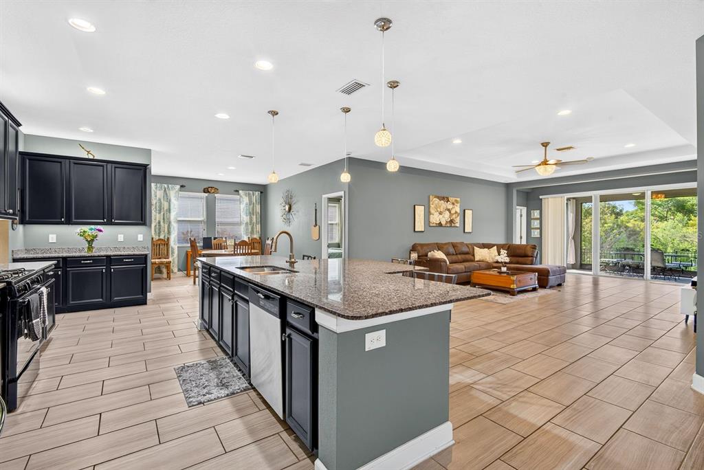 An open-concept kitchen with dark cabinets and a granite island flows into a living area — 792 ROSEMARY CIRCLE, BRADENTON, FL