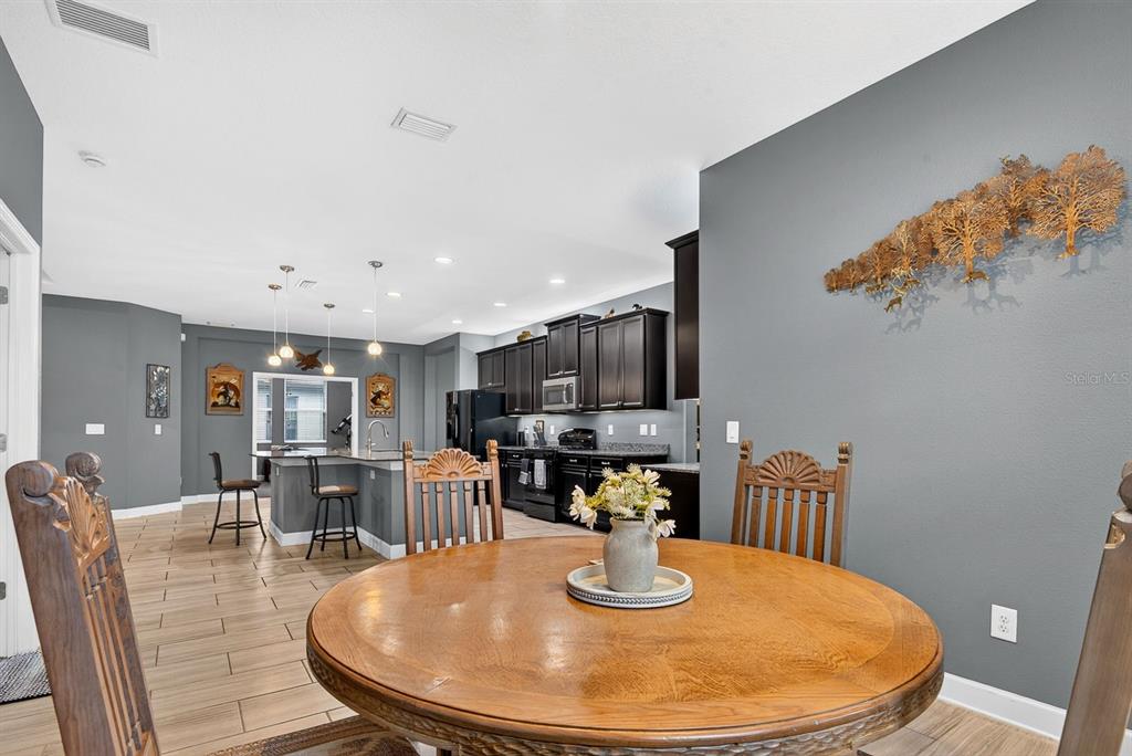 A dining area with a round wooden table leads into a kitchen with dark cabinetry — 792 ROSEMARY CIRCLE, BRADENTON, FL