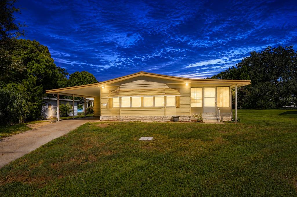 A single-story house with light yellow siding, a carport, and a front porch at dusk — 3417 WAX MYRTLE CIRCLE, ZELLWOOD, FL
