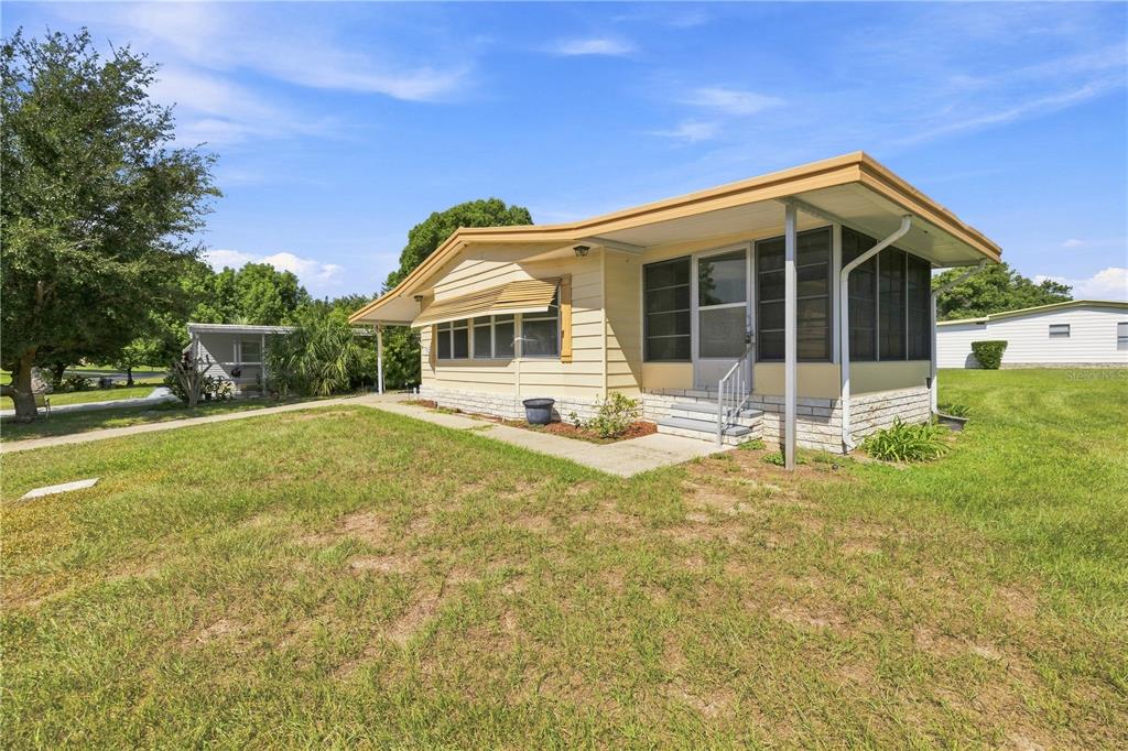 A single-story mobile home with yellow siding, a screened-in porch, and a grassy yard — 3417 WAX MYRTLE CIRCLE, ZELLWOOD, FL