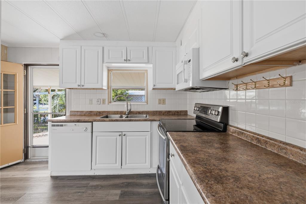 A kitchen features white cabinets, brown laminate countertops, a stainless steel stove, and wood-look flooring — 3417 WAX MYRTLE CIRCLE, ZELLWOOD, FL