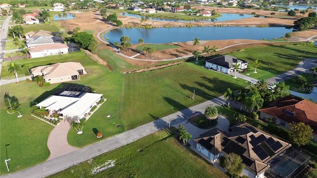 An aerial view shows a vacant residential lot situated between two houses near a lake — 18001 BLUEWATER DRIVE, NAPLES, FL