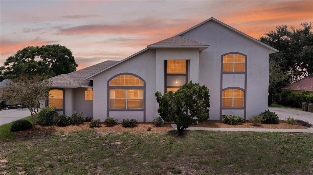 A two-story house with a stucco exterior, arched windows, and a shingled roof at sunset — 12608 LAKE RIDGE CIRCLE, CLERMONT, FL