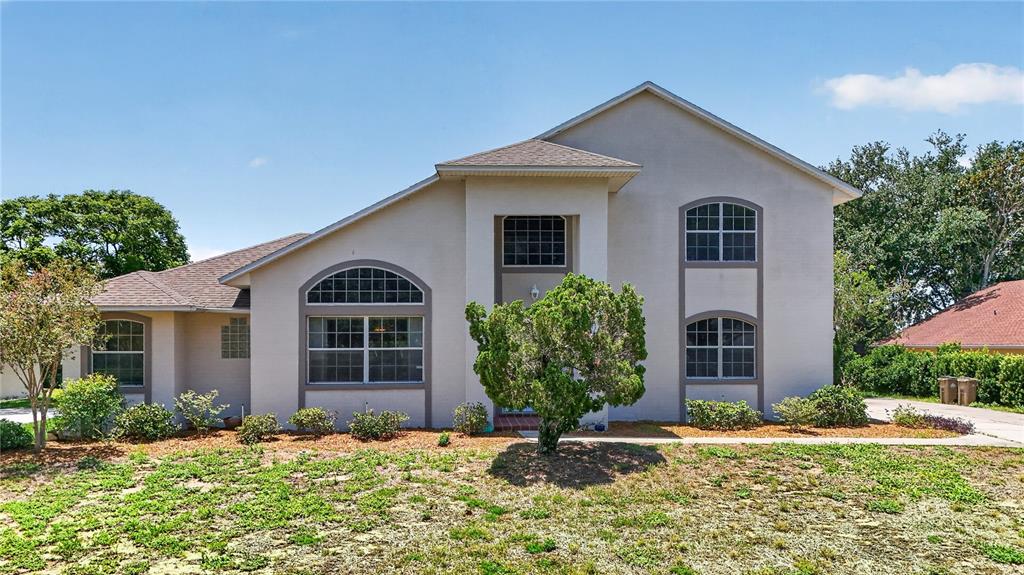 A two-story beige house with a front-facing gable and arched windows sits on a lawn — 12608 LAKE RIDGE CIRCLE, CLERMONT, FL