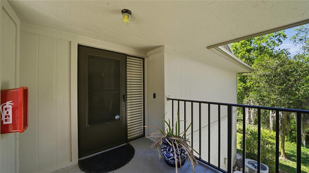 An exterior view of a covered apartment balcony with a front door and fire extinguisher — 32 NAVARRA COURT, ST AUGUSTINE, FL