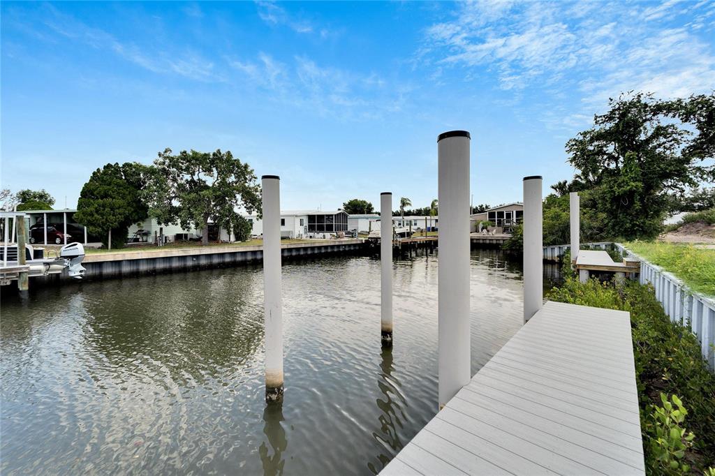 A wooden dock extends into a canal lined with tall pilings and residential mobile homes — 6540 SIMONE SHORES CIRCLE, APOLLO BEACH, FL