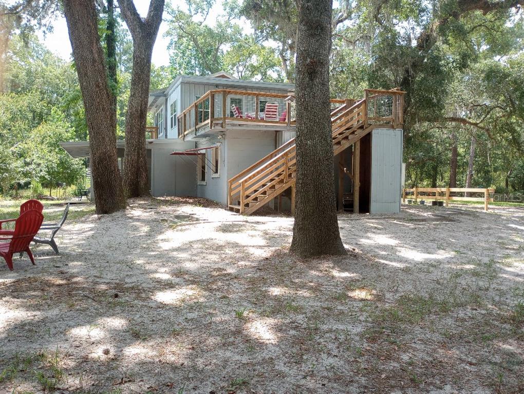 A two-story house with a large wooden deck and exterior staircase sits in a sandy yard — 348 NW NULL ROAD, WHITE SPRINGS, FL