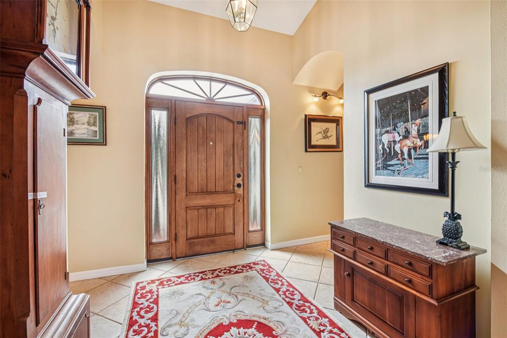 A foyer features a wooden front door, a patterned rug, and a marble-topped console table — 8013 PINE HOLLOW DRIVE, MOUNT DORA, FL
