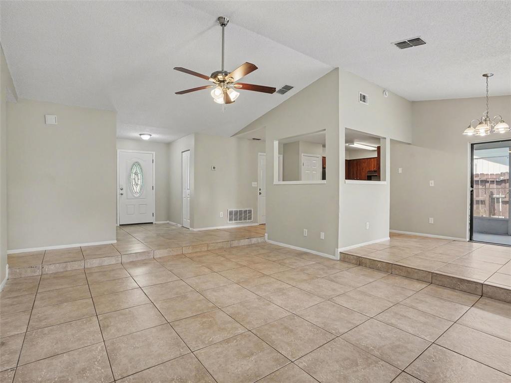 An open-concept living area features beige tile flooring, a vaulted ceiling, and a ceiling fan — 3329 FOX RIDGE DRIVE, WINTER HAVEN, FL
