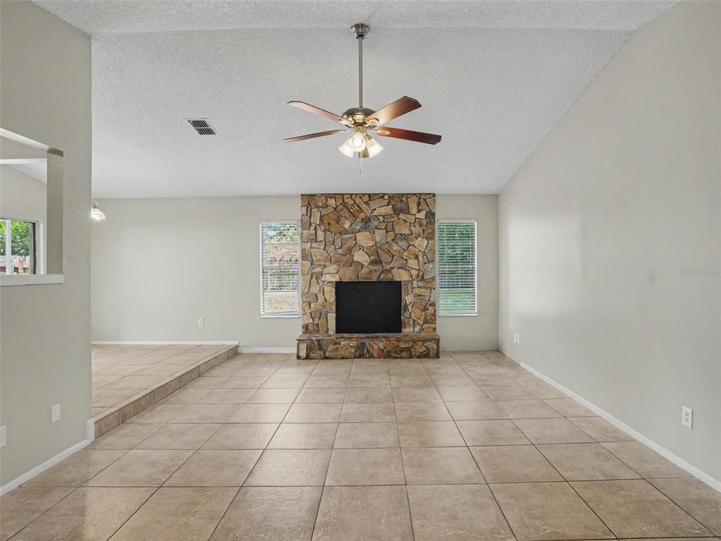 A living room features a stone fireplace, tile flooring, and a ceiling fan — 3329 FOX RIDGE DRIVE, WINTER HAVEN, FL