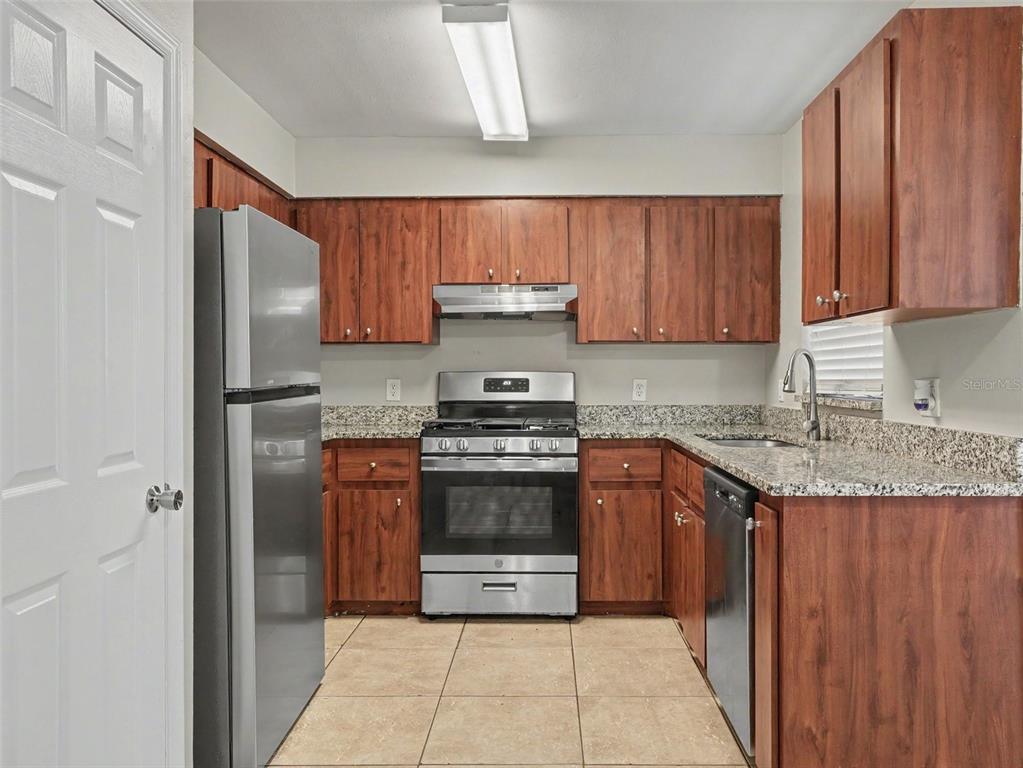 A kitchen features wood cabinets, granite countertops, stainless steel appliances, and beige tile flooring — 3329 FOX RIDGE DRIVE, WINTER HAVEN, FL