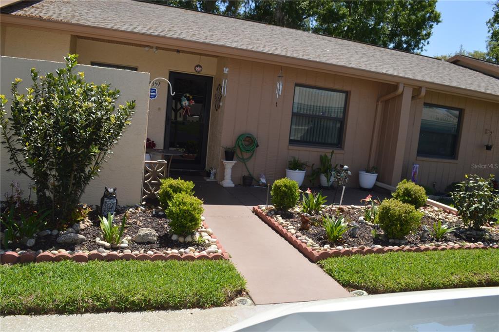 A tan single-story house features a concrete walkway leading to a front entrance with landscaping — 38359 IRONWOOD PLACE UNIT 38359, ZEPHYRHILLS, FL