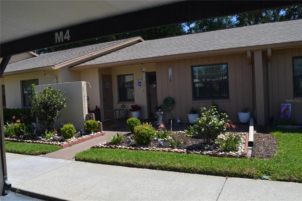 A single-story residential unit features a covered entryway, a small front garden, and a carport — 38359 IRONWOOD PLACE UNIT 38359, ZEPHYRHILLS, FL