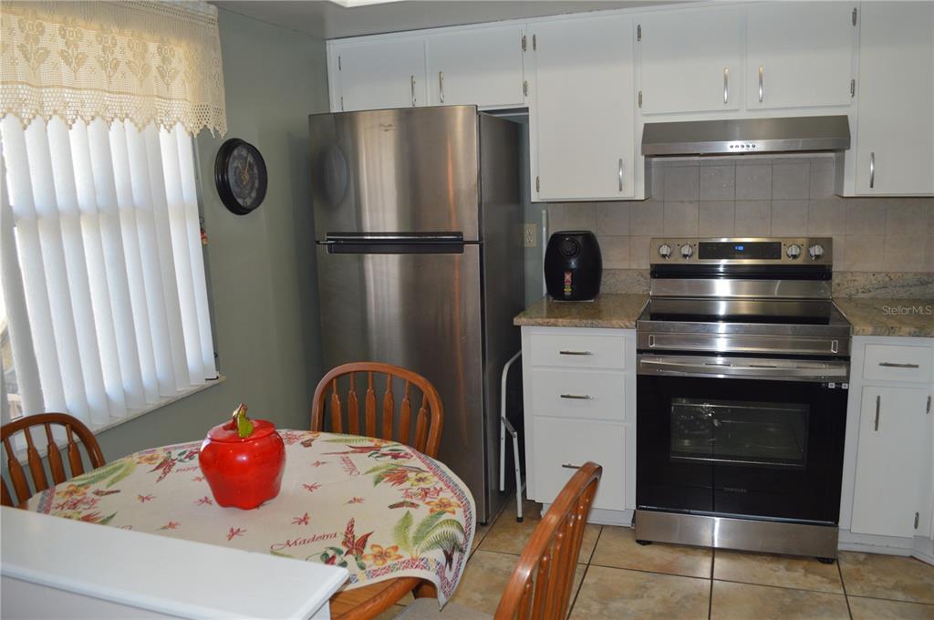 A kitchen features white cabinets, stainless steel appliances, tile flooring, and a small dining table — 38359 IRONWOOD PLACE UNIT 38359, ZEPHYRHILLS, FL