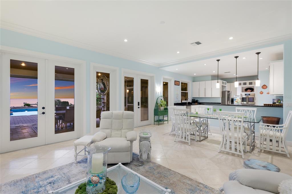 A bright open-concept living and dining area features tile floors, white furniture, and glass doors — 518 58TH STREET, HOLMES BEACH, FL