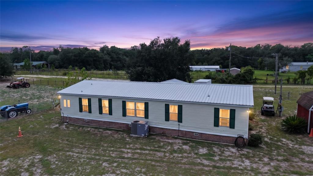 An aerial view of a single-story manufactured home with a metal roof at sunset — 15355 SE 113TH STREET ROAD, OCKLAWAHA, FL
