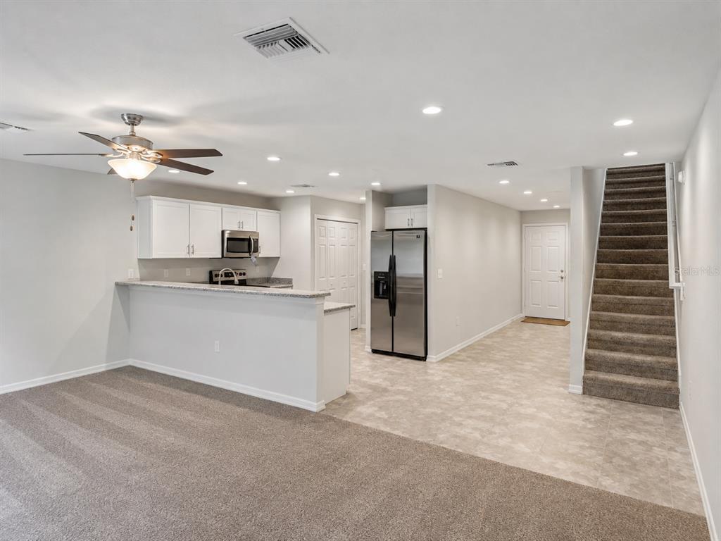 A kitchen with white cabinets and stainless steel appliances overlooks a carpeted living area — 13120 SONOMA BEND PLACE, GIBSONTON, FL