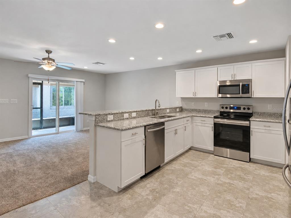 A kitchen with white cabinets, granite countertops, and stainless steel appliances overlooks a carpeted living area — 13120 SONOMA BEND PLACE, GIBSONTON, FL