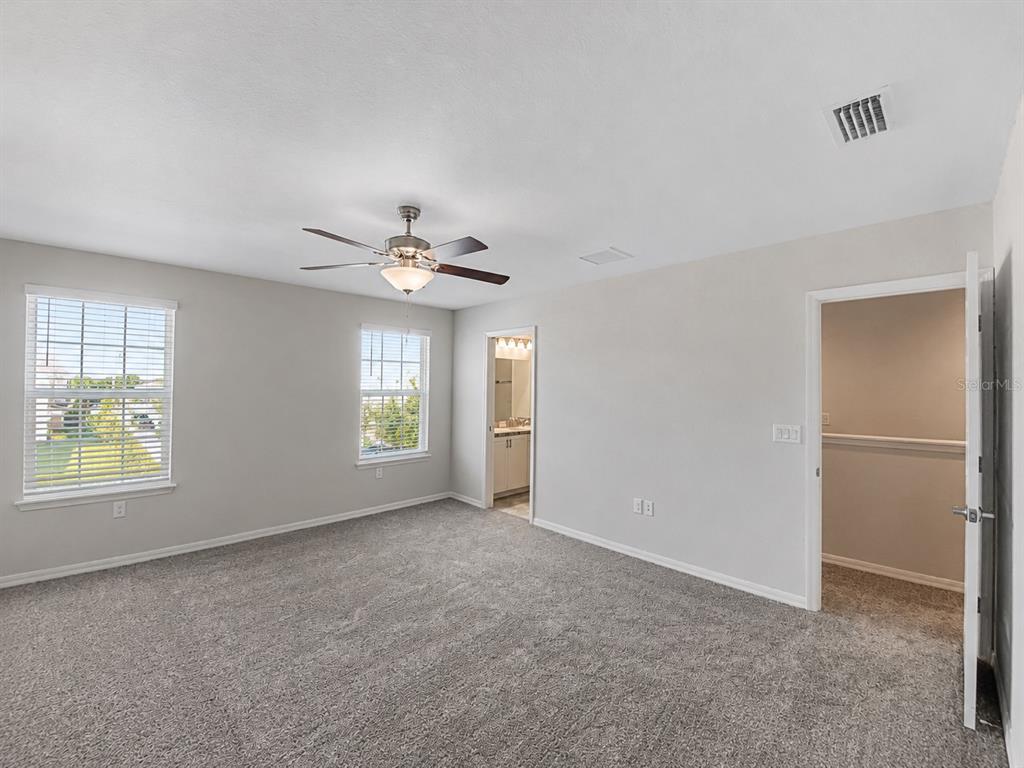 A carpeted bedroom features two windows, a ceiling fan, and doorways leading to other rooms — 13120 SONOMA BEND PLACE, GIBSONTON, FL