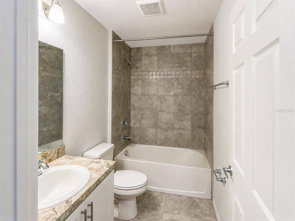 A bathroom features a vanity with a stone countertop, a toilet, and a tiled tub-shower — 13120 SONOMA BEND PLACE, GIBSONTON, FL