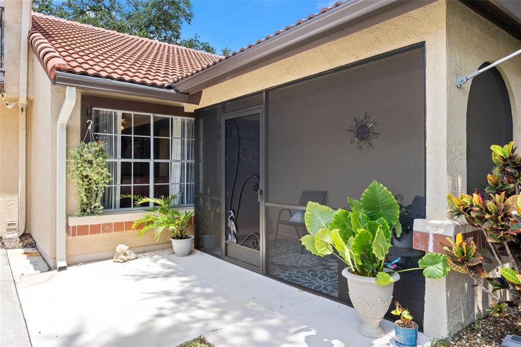 A concrete patio leads to a screened-in porch with a decorative door and tiled roof — 898 BROW COURT NE, PALM BAY, FL