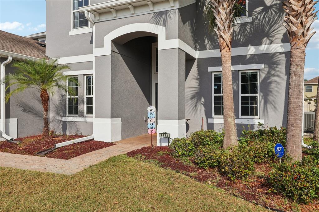 The exterior of a two-story gray house features a covered entryway, palm trees, and landscaping — 2132 PLANTATION OAK DRIVE, ORLANDO, FL
