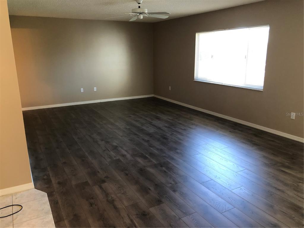 An empty living room features dark wood-look flooring, beige walls, and a ceiling fan — 17513 SE 95TH COURT, SUMMERFIELD, FL