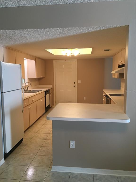 A kitchen with light wood cabinets, white appliances, a breakfast bar, and tile flooring — 17513 SE 95TH COURT, SUMMERFIELD, FL