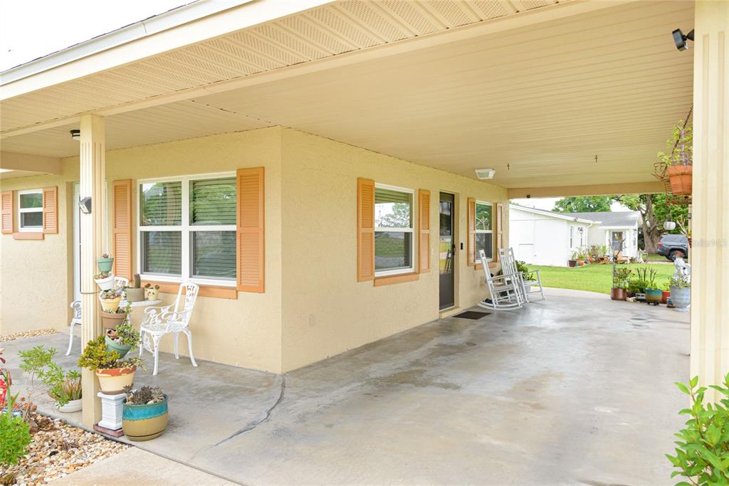 A covered concrete patio area features a yellow stucco exterior, white shutters, and rocking chairs — 2300 3RD STREET, ST CLOUD, FL