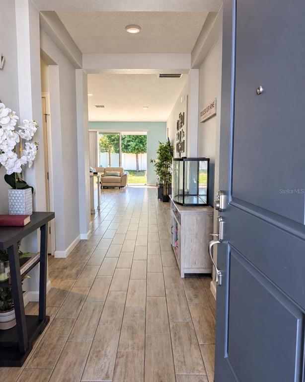 An entryway with wood-look tile flooring leads into a living area with a sliding glass door — 2913 BLUESTEM LANE, CLERMONT, FL